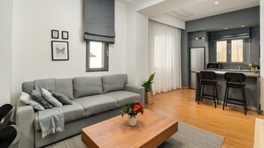 A modern living room with a grey sofa, a wooden coffee table, and a kitchen area with a microwave and bar stools. - Entire 2nd-Floor Home · 3 Bedrooms · Sleeps 7 · Central Athens, Private Terrace (Athina)
