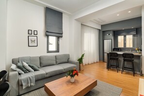 Ein modernes Wohnzimmer mit einem grauen Sofa, einem Holztisch und einer Küchenzeile mit Mikrowelle und Barhocker.