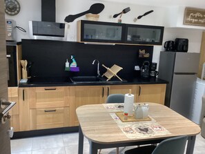 Eine kleine Küche mit schwarzer Arbeitsplatte, Holzschränken, einem Spülbecken und einer Essecke mit Tisch für zwei Personen.
