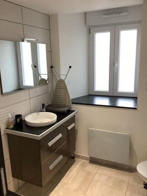 Casa de banho moderna com lavatório branco, armários escuros, espelho e janela com molduras brancas.