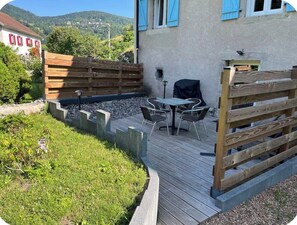 A wooden deck with a table and chairs, a covered grill, and a view of a hillside. - Perfect 2-bedroom apartment in enjoyable Bussang for your getaway (Bussang)