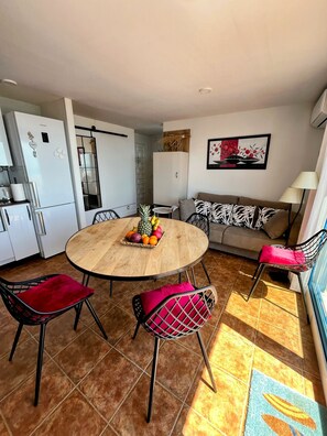 A compact living space with a round wooden dining table, two chairs, a sofa, and a kitchenette. - Mirador of the Mediterranean, (Peñíscola)