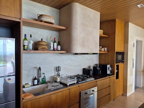A modern kitchen with wooden cabinets, a stainless steel refrigerator, a built-in oven, and a microwave. - Uluviu Villa (Badung)