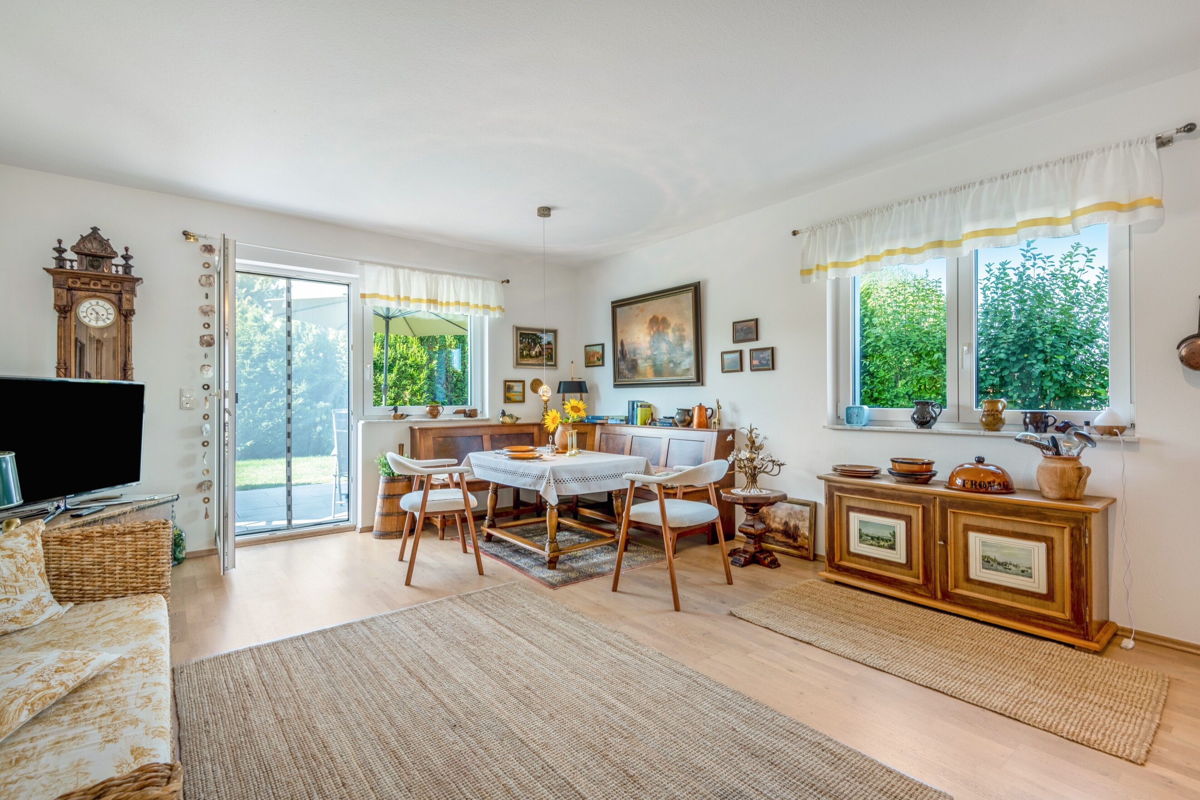 A spacious living room with a dining area, a kitchen, and a large window providing a view of greenery.