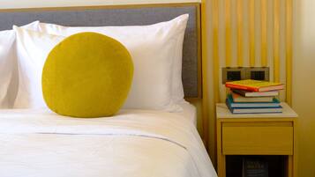 A bed with white bedding, a yellow pillow, and a bedside table with books and a 'SAVE WATER' sign.