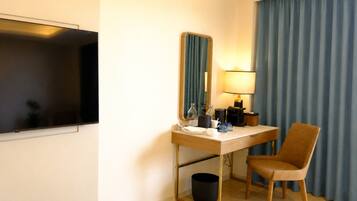Ein Hotelzimmer mit Schreibtisch, Stuhl, Fernseher, Spiegel, Lampe und Vorhängen.