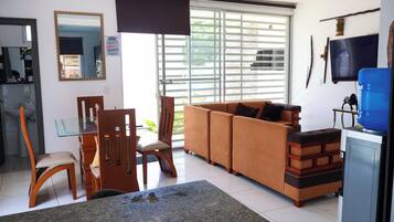 A living room with a sofa, chairs, a glass table, and a television.