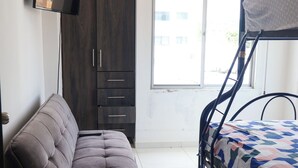 A bedroom with a sofa, bunk bed, wardrobe, and a TV.