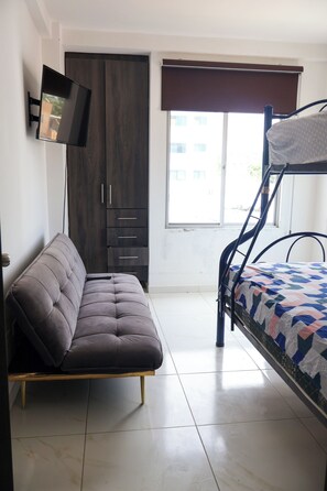 A bedroom with a sofa, bunk bed, wardrobe, and a TV.