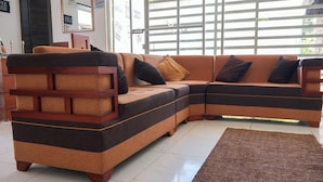 A sectional sofa with a wooden frame and cushioned seating, a brown rug, and a window with blinds.