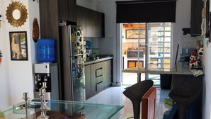 A modern kitchen with a glass dining table, wooden chairs, and a refrigerator with magnets.