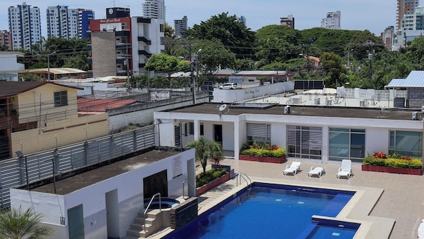 A rooftop swimming pool with a diving board, surrounded by lounge chairs and a small garden area.