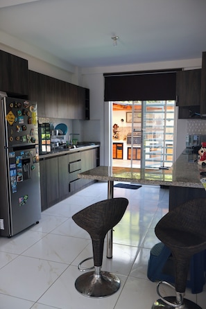 A modern kitchen with a refrigerator, microwave, and dining area with two bar stools.