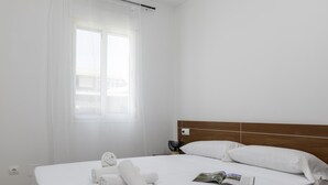 Ein Hotelzimmer mit Bett, Fenster mit Vorhängen, Nachttisch mit Lampe und einer Zeitschrift auf dem Bett.