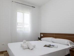 A hotel room with a bed, a window with curtains, a bedside table with a lamp, and a magazine on the bed. - Sunstay Pedregal A Flat I Málaga (Málaga)