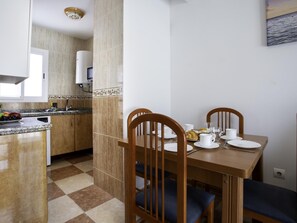 Ein Essbereich mit Holztisch und -stühlen, eine Küche mit Einbauherd und einer gefliesten Spritzschutzwand.