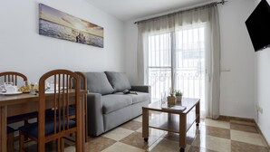 Ein Wohnzimmer mit einer Couch, einem Esstisch, Stühlen, einem kleinen Couchtisch, einem Gemälde und einem Fernseher.
