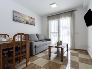 A living room with a sofa, dining table, chairs, a small coffee table, a painting, and a TV. - Sunstay Pedregal A Flat I Málaga (Málaga)