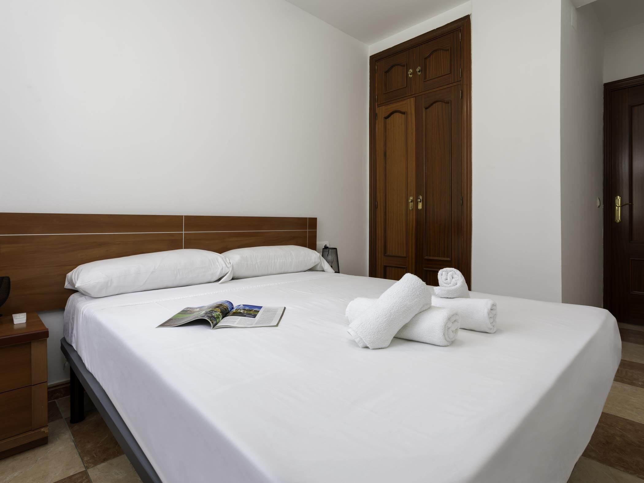 Een hotelkamer met een groot bed, een houten hoofdeinde, een kledingkast en een nachtkastje met een lamp.