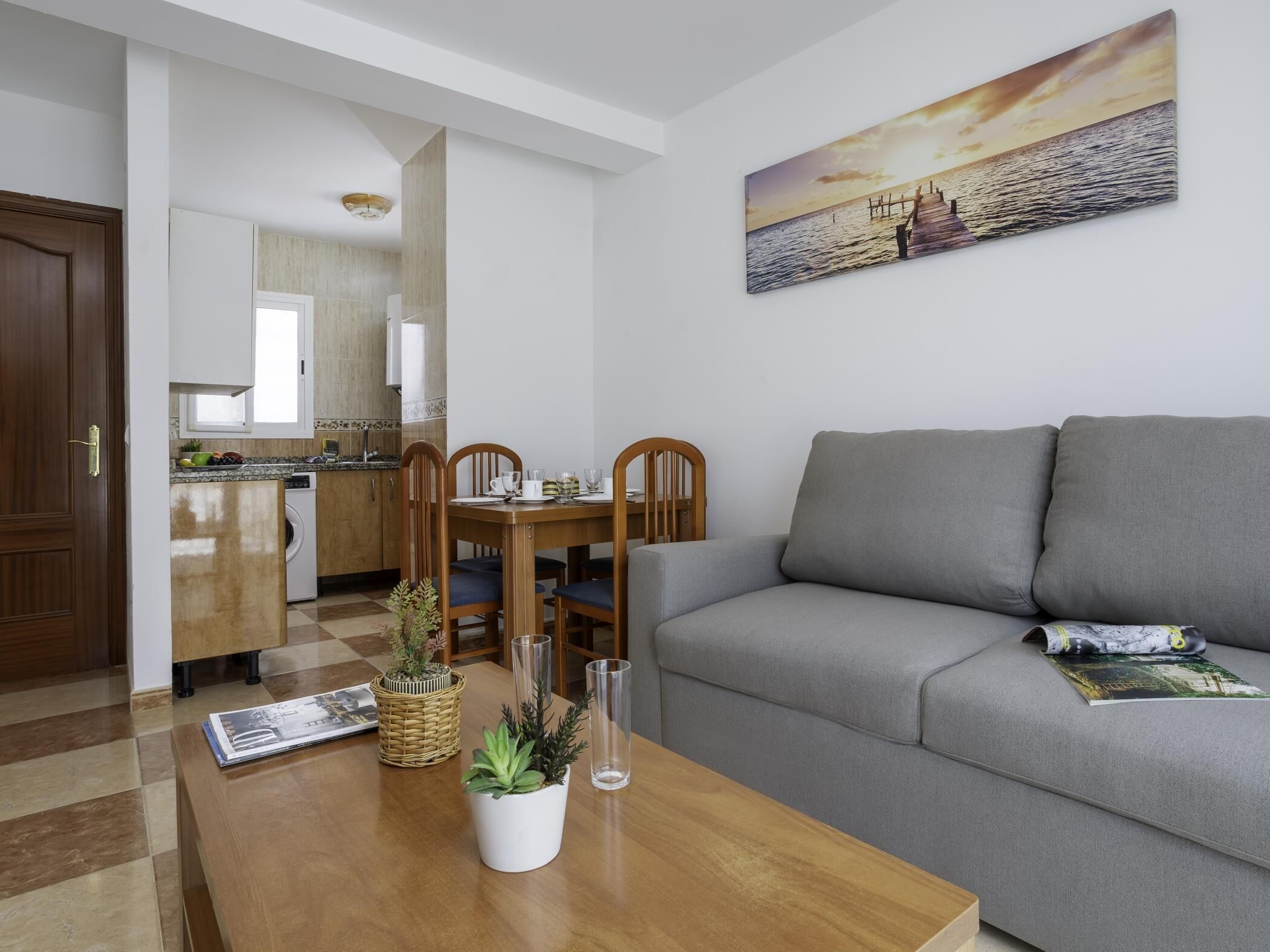 Un salon moderne avec un canapé gris, une table à manger en bois et une cuisine en arrière-plan.