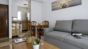 Ein modernes Wohnzimmer mit grauem Sofa, einem Holzesstisch und einer Küche im Hintergrund.