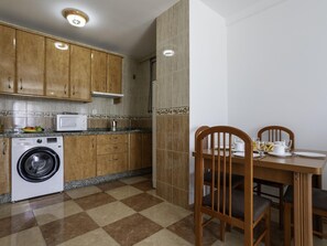 A kitchen with wooden cabinets, a washing machine, a microwave, and a dining area with a table and chairs. - Sunstay Pedregal C Flat I Málaga (Málaga)