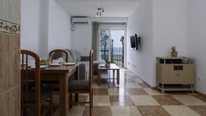 A dining area with a checkered floor, a wooden dining table with chairs, a sofa, and a TV mounted on the wall. - Sunstay Pedregal C Flat I Málaga (Málaga)