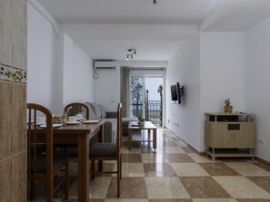 A dining area with a checkered floor, a wooden dining table with chairs, a sofa, and a TV mounted on the wall. - Sunstay Pedregal C Flat I Málaga (Málaga)