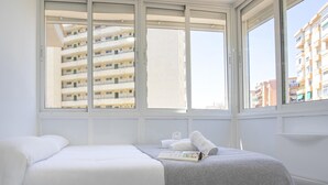 A bedroom with a bed, a bedside table, and a window with a view of a building. - Sunstay Lovely Loft Fuengirola (Fuengirola)