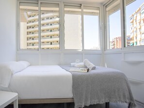 Ein Schlafzimmer mit Bett, Nachttisch und Fenster mit Blick auf ein Gebäude.