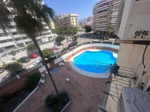 Ein Pool auf dem Dach mit klarem, blauem Wasser, umgeben von Liegestühlen und einer Palme.