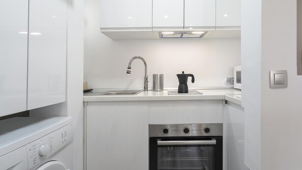 A modern kitchen with white cabinetry, a stainless steel sink, a coffee maker, a kettle, and an oven. - Sunstay Lovely Loft Fuengirola (Fuengirola)