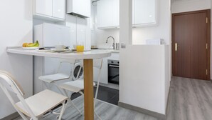 A compact kitchen with white cabinets, a sink, a washing machine, and a dining area with a table and chairs. - Sunstay Lovely Loft Fuengirola (Fuengirola)