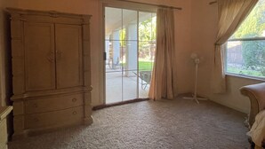 A room with a large wooden wardrobe, a sliding glass door leading to an outdoor patio, and a window with curtains. - Perfect for a traveling professional! (Clovis)