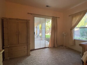 A room with a large wooden wardrobe, a sliding glass door leading to an outdoor patio, and a window with curtains. - Perfect for a traveling professional! (Clovis)