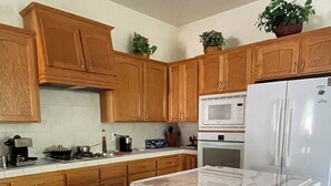 A kitchen with wooden cabinets, a central island, a refrigerator, and a microwave. - Perfect for a traveling professional! (Clovis)
