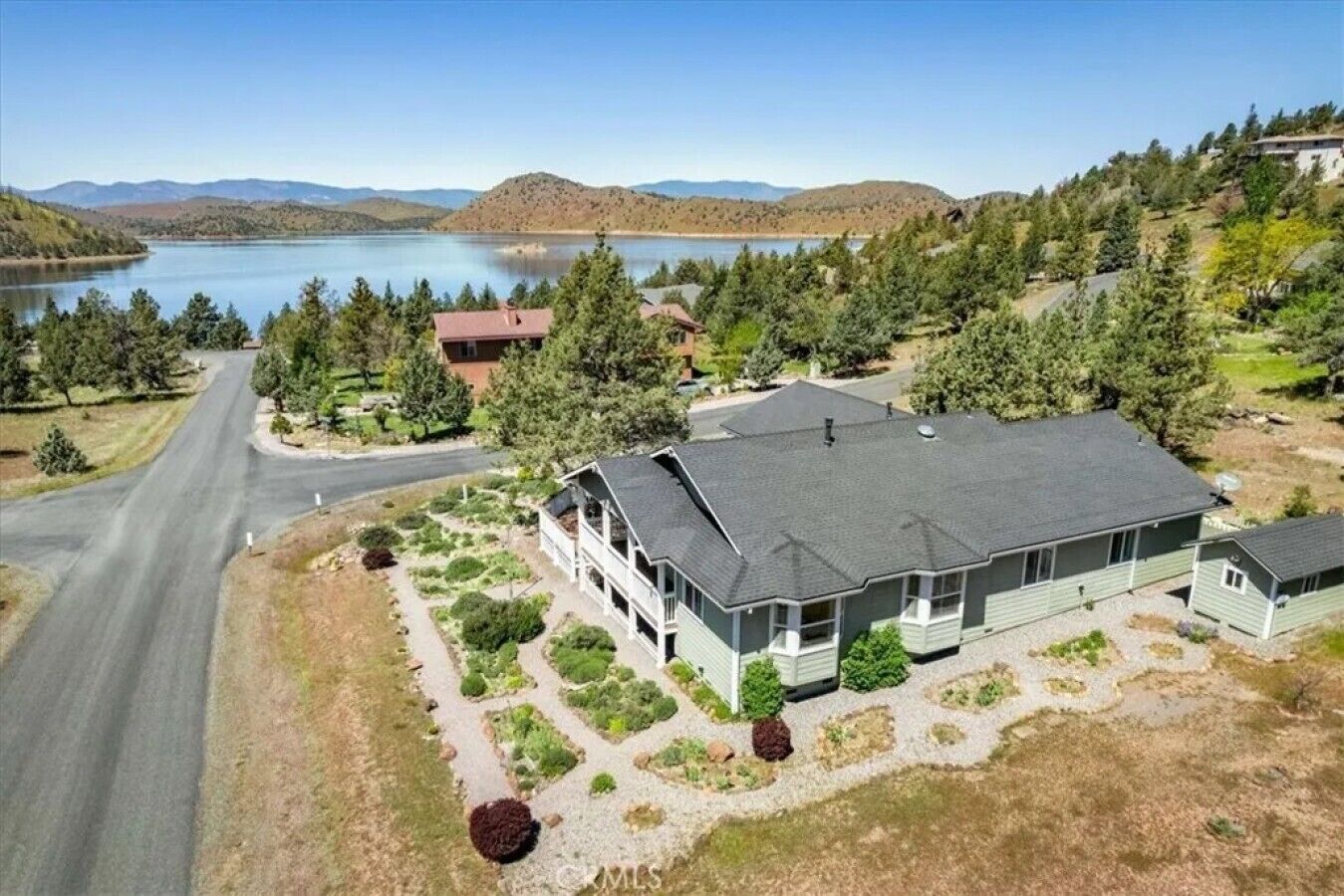 A two-story house with a large front lawn, a driveway, and a lake in the background.