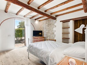 A bedroom with a stone wall, wooden beams, a bed, a TV, and a view of the outdoors. - The San Leonino House (Castellina in Chianti)