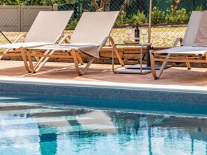 A poolside area with lounge chairs and a table, a bottle of wine, and glasses. - The San Leonino House (Castellina in Chianti)