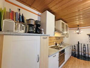 A kitchen with white cabinets, a stove, a sink, and a coffee maker. - Prien Vacation Rental for 2 People with a Separate Bedroom and North-Facing Balcony, 40 square meters, No. 1 (Aschau im Chiemgau)