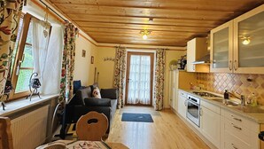 Un accogliente interno di una baita con soffitto in legno, un'area pranzo con tavolo e sedie, un soggiorno con divano e una cucina con mobili ed elettrodomestici.