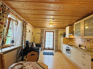 Ein gemütliches Blockhaus-Interieur mit Holzbalkendecke, einem Essbereich mit Tisch und Stühlen, einem Wohnzimmer mit einer Couch und einer Küche mit Schränken und Geräten.