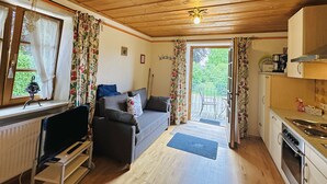 Interno accogliente di una baita con zona soggiorno, angolo pranzo e vista attraverso la porta.