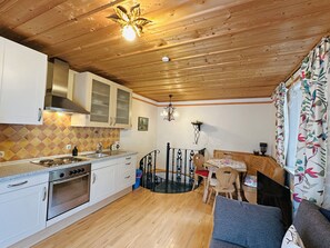 A kitchen with wooden cabinets, a stove, and a dining area with a table and chairs. - Prien Vacation Rental for 2 People with a Separate Bedroom and North-Facing Balcony, 40 square meters, No. 1 (Aschau im Chiemgau)