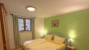Ein Schlafzimmer mit einem Bett, einem Nachttisch, einem Fenster mit Vorhängen, einer Heizung und einem Bild an der Wand.
