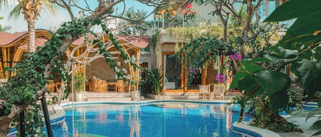 Uma piscina rodeada por plantas tropicais e mobiliário de madeira.