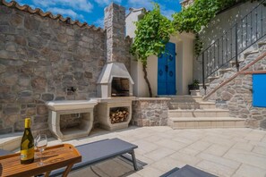 A stone-walled outdoor area with a stone fireplace, a blue door, and a staircase. - Holiday Home in the Crikvenica Hinterland – Pool, Sauna & Complete Privacy (Tribalj)