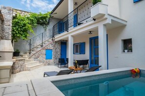 A poolside area with a stone staircase, a balcony with blue railings, and a table with chairs. - Holiday Home in the Crikvenica Hinterland – Pool, Sauna & Complete Privacy (Tribalj)