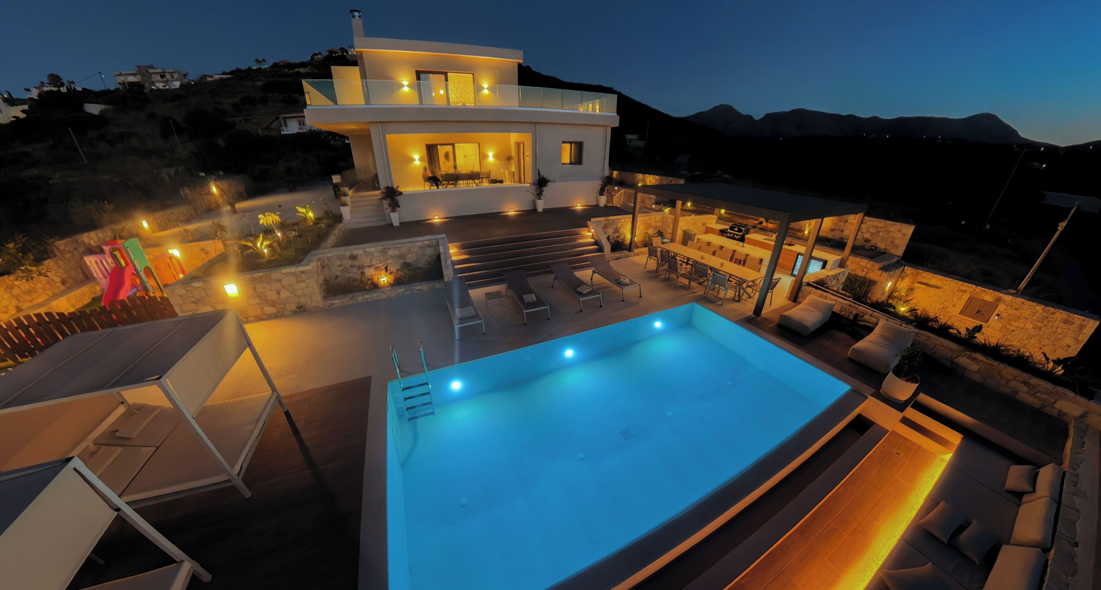 Une maison moderne à deux étages, dotée d’une piscine, d’un espace salon extérieur et offrant une vue sur les montagnes.