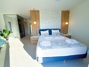 A modern bedroom with a large bed, bedside tables, a wall-mounted light, and a decorative panel. - Cozy Villa Kissamos (Kissamos)